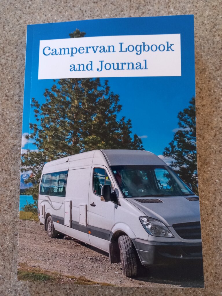 This photo shows the front cover of my campervan journal. It shows a grey campervan parked in front of trees.