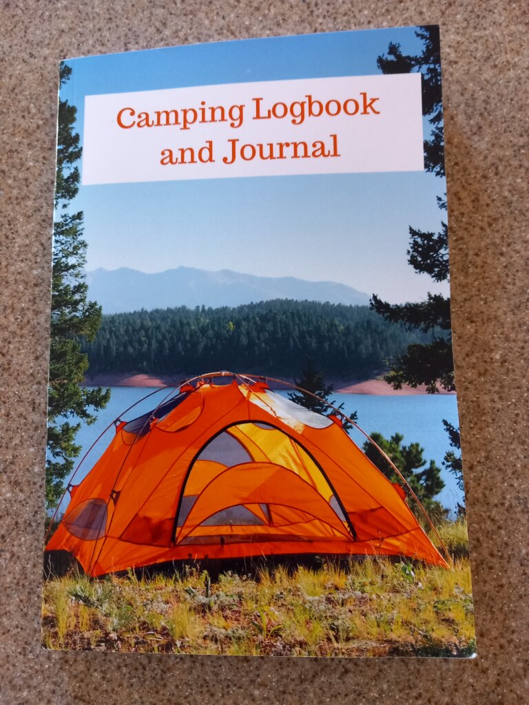 This photo shows the front cover of my camping journal. It shows an orange tent pitched in front of a lake