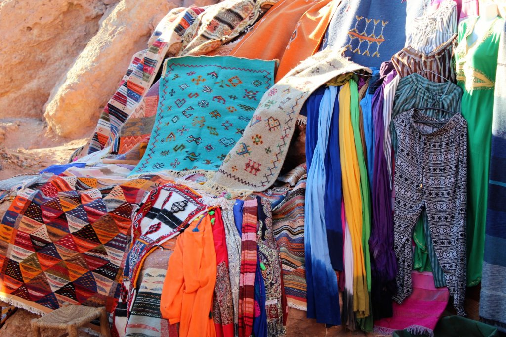 This photo shows colourful carpets and clothing on sale in Ait Benhaddou
