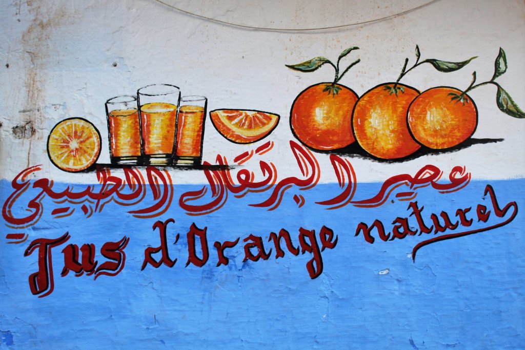 This photo shows hand painted oranges and glasses of orange juice on a blue and white painted wall